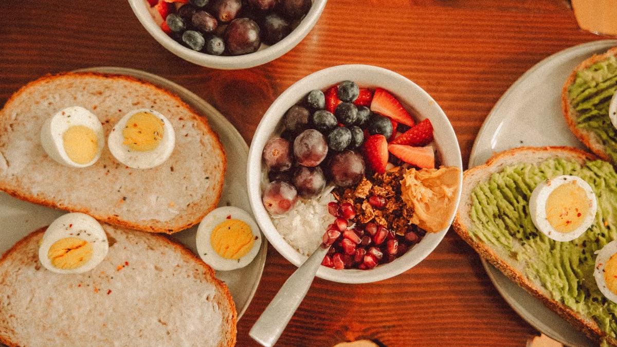 A fresh and vibrant breakfast flat lay featuring a yogurt bowl with fruits and toast with eggs and avocado.